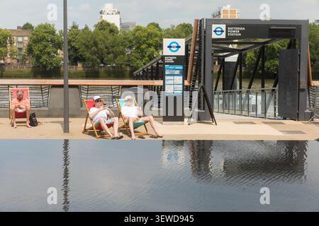Men relax in deckchairs at Nina Elms, Wandsworth, London, enjoying the sunshine by the iconic Battersea Power Station river pier. Stock Photo