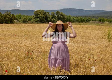 Woman in summer dress walking through golden wheat field under stormy sky. Stock Photo