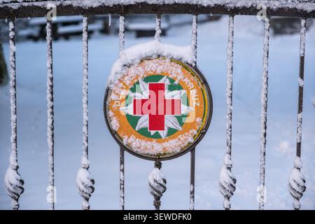 Snow-dusted German Red Cross Bergwacht emblem on a wrought iron fence in winter, ideal for rescue service and seasonal editorial use. Stock Photo
