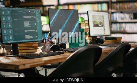 Multiple computer monitors show chatbot and blue presentation screen, digital content on interfaces at library study desk. Workspace with books, green lamps and keyboards. Stock Photo
