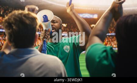 African american man chants through megaphone in football stadium stands during match. Fan leader galvanizing soccer supporters to create loud atmosphere and strong team support Stock Photo