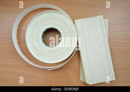 A top-down view of vintage computer data storage media, featuring a roll of punched paper tape and a stack of punch cards on a wooden surface Stock Photo