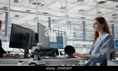 Reviewing microchip production operations, PC software and man with woman inside factory workplace. Improving semiconductor hardware performance, work and experts in RD office, camera A Stock Photo