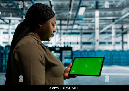 System operator uses a green screen tablet in a data center for failure detection, screen replacement, and server workflow monitoring. Stock Photo