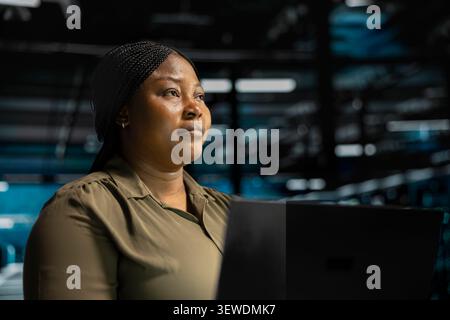 System administrator uses a laptop computer in a data center to monitor equipment, manage workflows, and support reliable infrastructure. Stock Photo