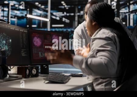 Pensive data center technicians review system data in a data center while planning repairs for performance and hardware issues. Stock Photo