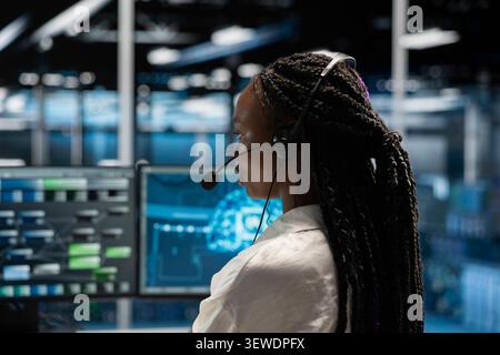 African American woman wears a headset in a server room, using artificial intelligence troubleshooting to assist users. Stock Photo
