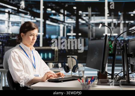 Female IT worker reviews performance analytics on a desktop computer in a data center to optimize storage systems and resource use. Stock Photo