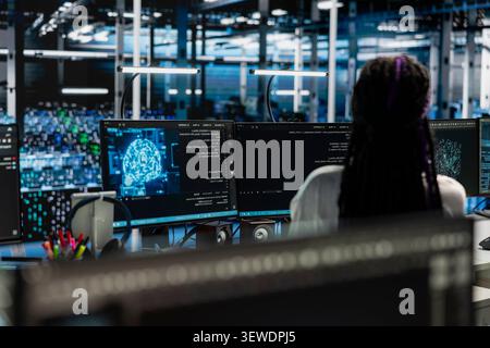 Female technician uses a desktop computer in a data center to manage AI systems and optimize server infrastructure. Stock Photo
