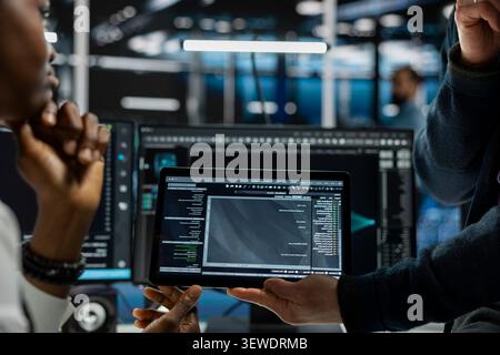 Data center programmers use a digital tablet in a data center to run hardware diagnostics and maintain operational stability. Stock Photo