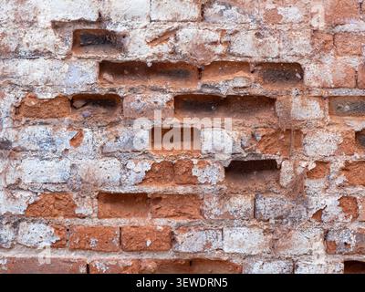 Old brick wall with peeling paint and missing bricks creating a weathered texture Stock Photo