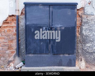 Dark metal electrical box mounted against a damaged urban wall Stock Photo