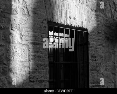 Stone wall framing a barred window, light and shadow creating contrast Stock Photo