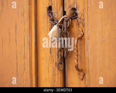 Weathered wooden door secured with a rusty metal chain and brass padlock Stock Photo