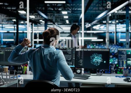 Engineer stretches at a workstation in a server hub to relieve back fatigue after long technical work. Stock Photo