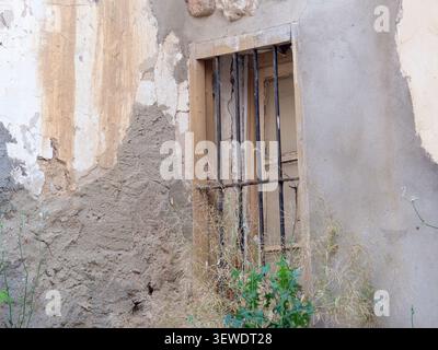 Old window on a decaying concrete wall with peeling paint and rusty bars Stock Photo