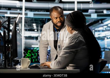 Data center colleagues collaborate on coding and AI automation scripts while reviewing server infrastructure together. Stock Photo