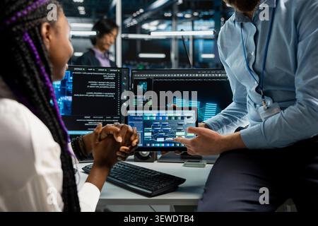 Data center programmer reviews AI systems and neural network parameters on a tablet inside a data center. Stock Photo