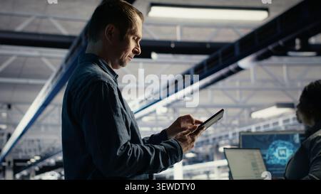Data center programmer reviews AI systems and neural network parameters on a tablet inside a data center. Stock Photo