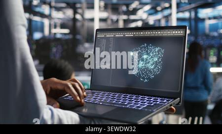 Data center technician monitors AI systems and machine learning workloads on a laptop inside a high-tech server facility. Stock Photo