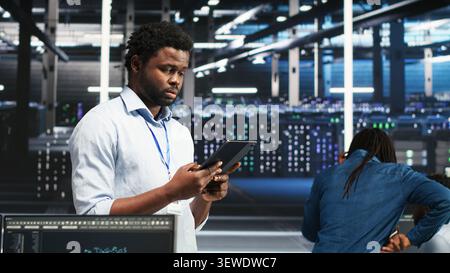 Data center technician uses a tablet with node tree programming to optimize resource allocation and analytics. Stock Photo