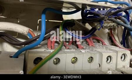 Close-up of a disorganized residential electrical breaker box with tangled red, blue, and green-yellow wires connected to terminals. Stock Photo