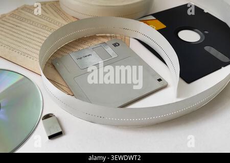 Collection of vintage data storage media: floppy disks, punch tape, CD, and USB drive. Evolution of computing hardware and archival information techno Stock Photo