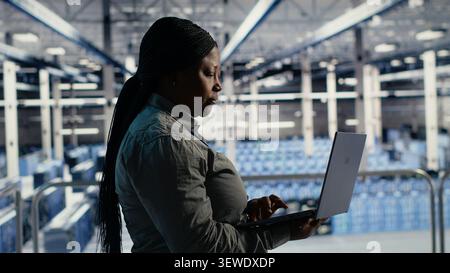 African american IT professional uses a laptop in a server room to review test results and confirm reliable system operation. Stock Photo