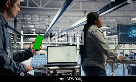 Software developer uses a green screen smartphone in a server room while waiting for code updates to finish. Stock Photo