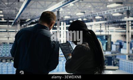 Data center colleagues respond to a warning alert on a laptop while troubleshooting server room systems. Stock Photo