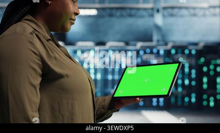 Software developer uses a green screen tablet in a server room for AI workflow and screen replacement. Stock Photo