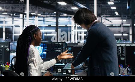 Asian man programs on a computer workstation in a data center with generative AI assistance. Stock Photo