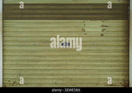 A full front view of a vintage, weathered green metal rolling shutter gate of a closed traditional shop or garage. Stock Photo
