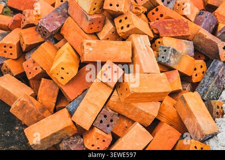 A high-angle shot of a messy heap of orange and red rectangular clay bricks with holes stacked on the ground. Stock Photo