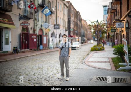 A man stands on a historic cobblestone street lined with old brick buildings and shops under warm evening light. Stock Photo