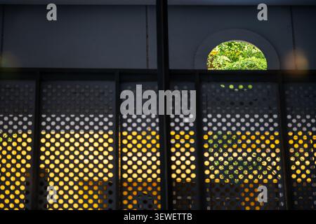 This modern metal gate features a perforated pattern with a circular window, allowing sunlight to filter through, creating shadows and an urban aesthe Stock Photo