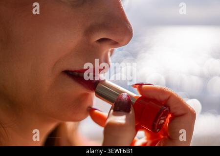 Lipstick red makeup close up of woman applying vibrant cosmetic to her lips against a sparkling bokeh background Stock Photo