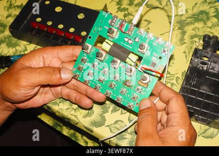 Close up of technician hands holding and inspecting a green printed circuit board of an audio electronic device. Stock Photo