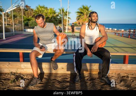 Two men resting on bench by basketball court Stock Photo
