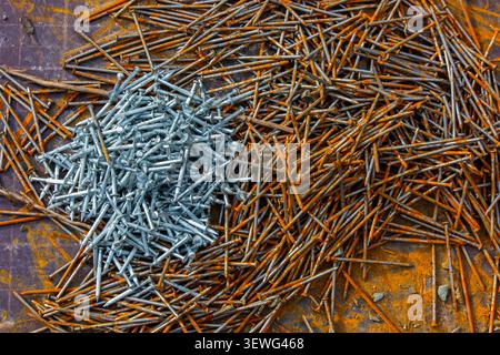 Overhead view features a pile of nails divided into two sections. Shiny silver nails on the left contrast with rusty orange nails on the right, highli Stock Photo