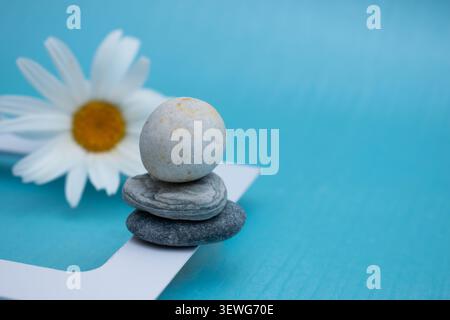 Balanced zen stones with white daisy on blue background Stock Photo