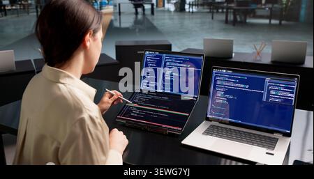 Young Female Software Developer Reviews Code Changes On Dual Touchscreen Laptops. Stock Photo