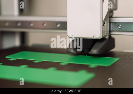 3D printer nozzle printing green plastic components on dark build plate Stock Photo