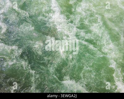 Close-up view of turbulent green water with white foam and swirling patterns. Sunlight reflects off the surface, creating a dynamic and energetic scen Stock Photo