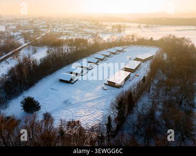 Aerial view of wooden frame houses in snowy landscape at sunset near village, showing winter construction progress, modern residential planning and eco friendly housing development Stock Photo