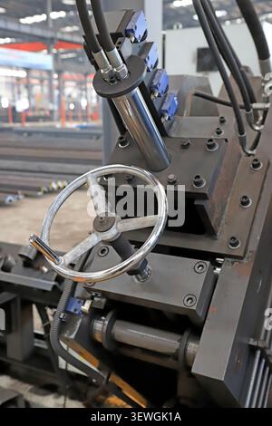 A high-resolution close-up of a precision industrial machine, featuring a polished metal manual steering wheel for adjustments, paired with hydraulic Stock Photo