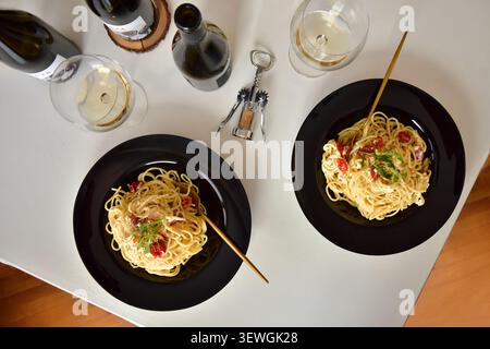 Homemade Italian spaghetti dinner for two in black plates with white wine on the table, top view Stock Photo