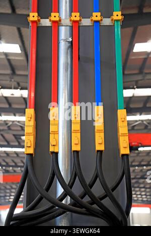 A high-resolution close-up of a color-coded industrial power busbar system, featuring red, blue, and green insulated conductors secured with bright ye Stock Photo