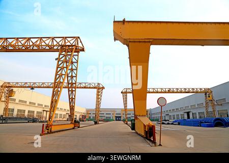 A wide-angle, eye-level view of a sprawling heavy machinery factory yard, featuring multiple towering orange gantry cranes of varying lattice and box- Stock Photo