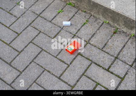 Iserlohn, Germany - June 16, 2026: Red Tic Tac "Fresh Orange" candy container and white object discarded on grey paved ground. Stock Photo